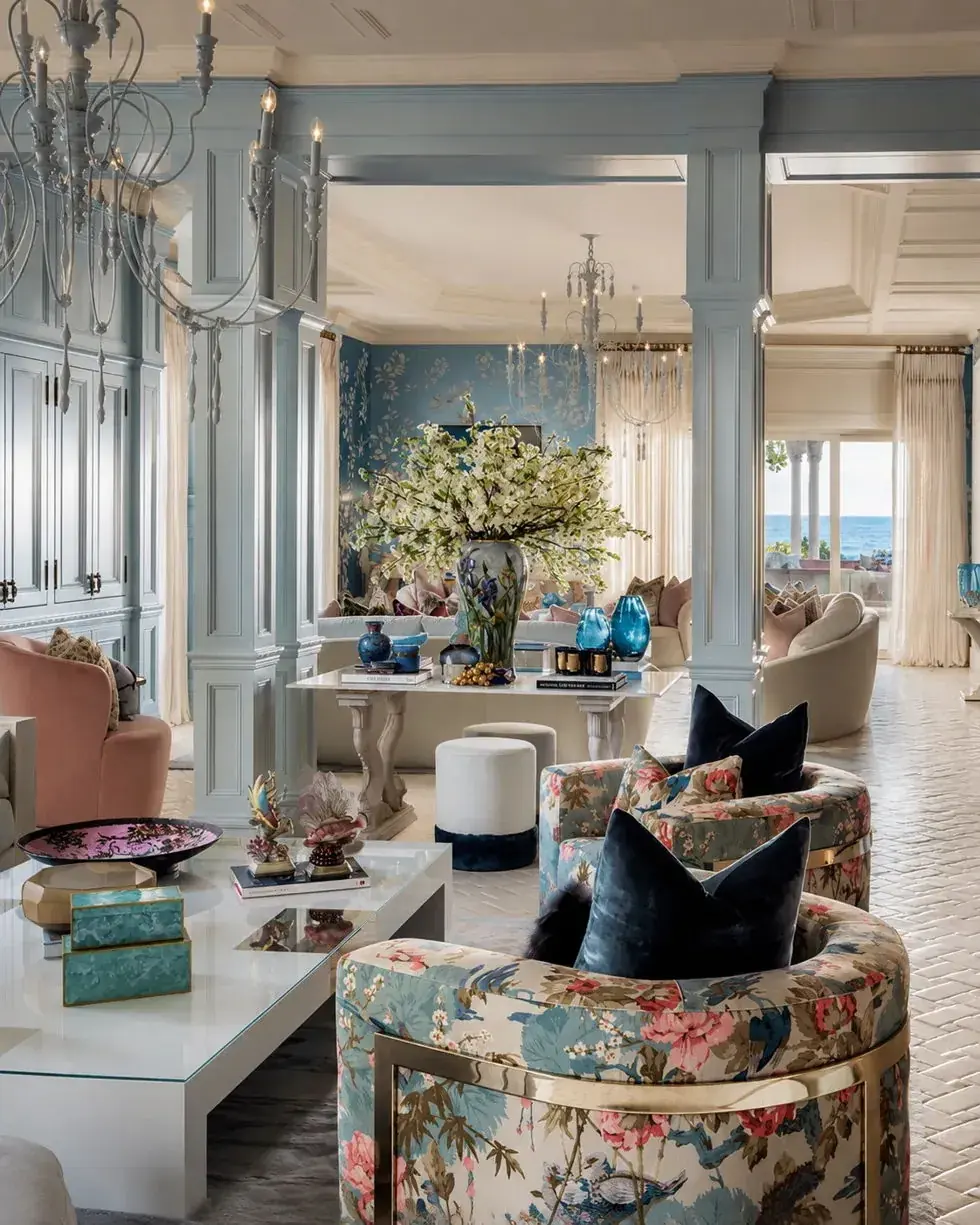 Coastal reception room with pale blue joinery, floral swivel chairs and chandeliers above a sea view